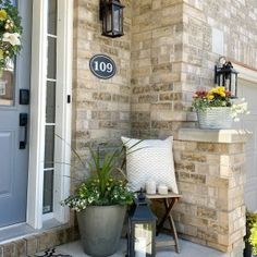 the front porch is decorated with potted plants and lanterns, along with an address sign