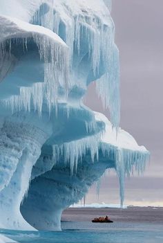 a boat is in the water next to an ice - covered rock formation with icicles hanging from it's sides