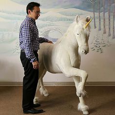 a man standing next to a white horse in front of a painting on the wall