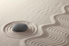 a rock sitting on top of a sandy beach next to a large wave pattern in the sand