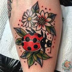 a ladybug tattoo on the leg with flowers