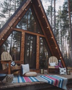 a small wooden cabin in the woods with lights on it's roof and two chairs