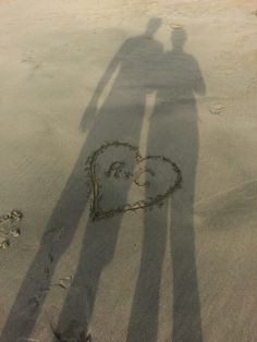 two people standing in the sand with a heart drawn on it