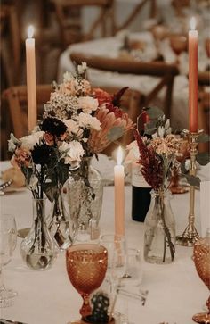 a table topped with lots of vases filled with flowers next to candles and wine glasses