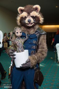 a man dressed as rocket raccoon holding a baby creature