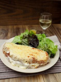 a white plate topped with an omelet next to a salad and glass of wine