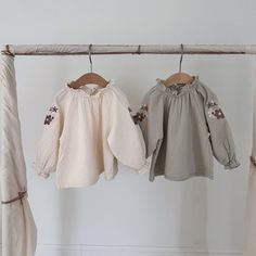 two baby blouses hanging on a clothes rack