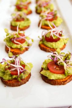 many small sandwiches with toppings on a white platter, ready to be eaten