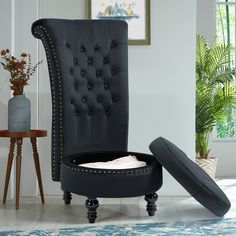 an upholstered black chair with buttons and studded trimmings sits next to a potted plant