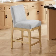 a kitchen with wooden floors and white counter tops on top of the floor is a light blue upholstered chair that sits in front of an island