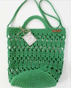 a green crocheted bag with a tag hanging from it's front pocket