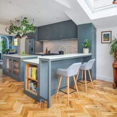 a kitchen with wooden floors and blue cabinets, white counter tops and two bar stools