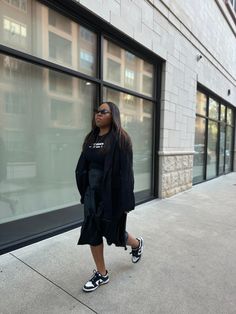 a woman is standing on the sidewalk in front of a building wearing black and white sneakers