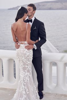 a man and woman standing next to each other in front of the ocean wearing wedding dresses