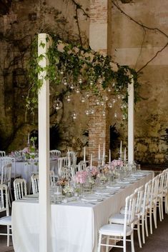 a long table is set up with white chairs and flowers in vases on the tables