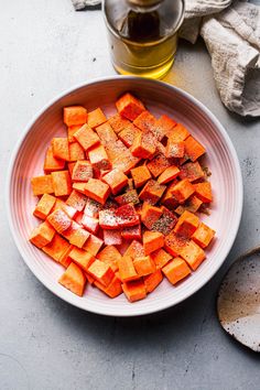 a white bowl filled with chopped up carrots next to a glass of honey syrup