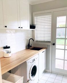 a washer and dryer in a white kitchen with wooden counter top next to sliding glass doors