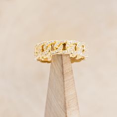 a yellow gold diamond ring on top of a wooden stand