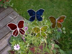 three stained glass butterflies sitting on top of a planter in the grass next to flowers