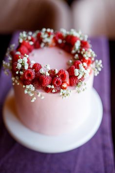 a pink cake with berries and baby's breath on top sitting on a table