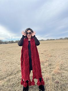 a woman standing in a field holding her hands up to the sky while wearing a red scarf