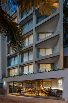 people sitting at tables in front of an apartment building with palm trees on the side