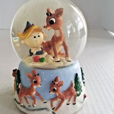 a snow globe with a girl and two deers in it on a white surface