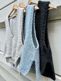 four knitted sweaters hanging on a clothesline in front of a white wall