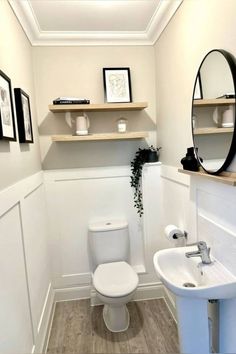 a white toilet sitting next to a sink in a bathroom under a mirror and shelves