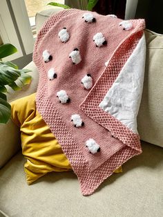 a pink and white blanket sitting on top of a couch next to a potted plant