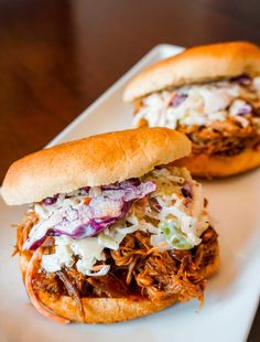 two pulled pork sandwiches with coleslaw and slaw on a white platter