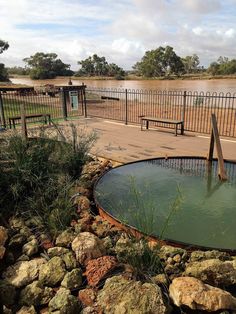 there is a small pond in the middle of some rocks and grass next to a fence