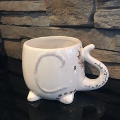 a white ceramic elephant mug sitting on top of a counter next to a stone wall