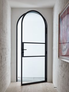 an arched glass door in the corner of a room with wooden floors and walls, leading to a painting on the wall