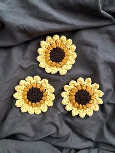 three crocheted sunflowers sitting on top of a black cloth covered bed