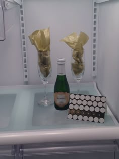 a bottle of champagne and two wine glasses on a shelf in a refrigerator with gold wrapping