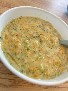 a white bowl filled with broccoli cheese soup on top of a wooden table