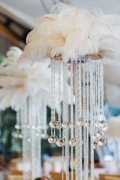 a chandelier with white feathers and beads hanging from it's sides in a room