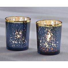 two blue candles with gold speckles are sitting on a gray tablecloth covered surface