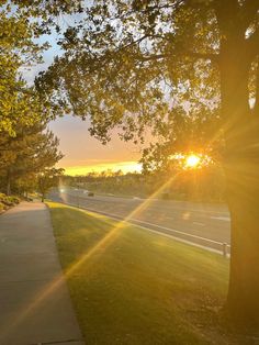 the sun shines brightly through the trees on this sidewalk in front of a street