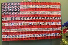 an american flag made out of newspaper strips hanging on a wall with flowers in the foreground