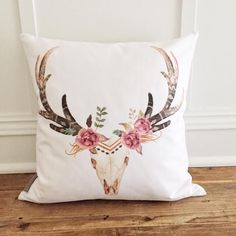 a white pillow with floral antlers on the front and back, sitting on a wooden floor