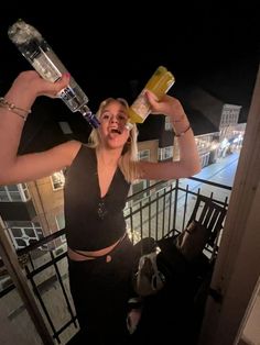 a woman is holding two bottles and posing for the camera with her arms in the air