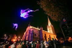 some people are flying kites in front of a building at night with lights on