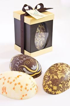 three decorated easter eggs in front of a gift box