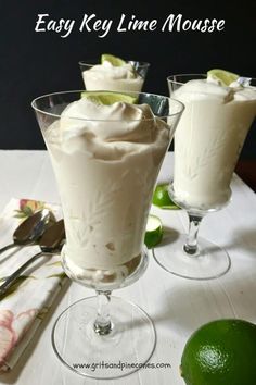 two glasses filled with dessert sitting on top of a table next to utensils