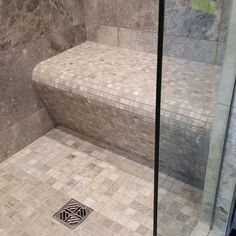 a walk in shower sitting next to a tiled wall and floor with a drain on the ground