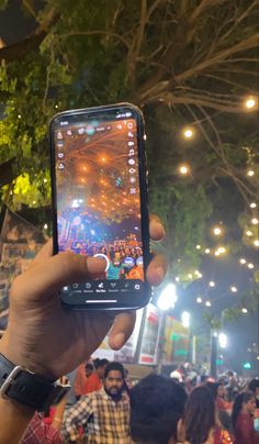 a person holding up a cell phone in front of a crowd at an outdoor event