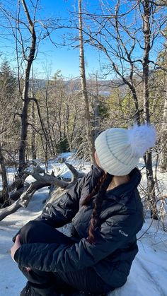 a woman sitting on top of a snow covered ground next to some bare trees in the woods