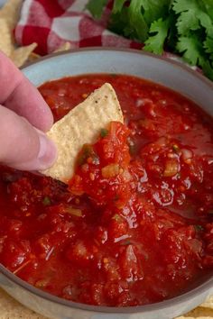 a hand dipping a tortilla chip into a bowl of salsa